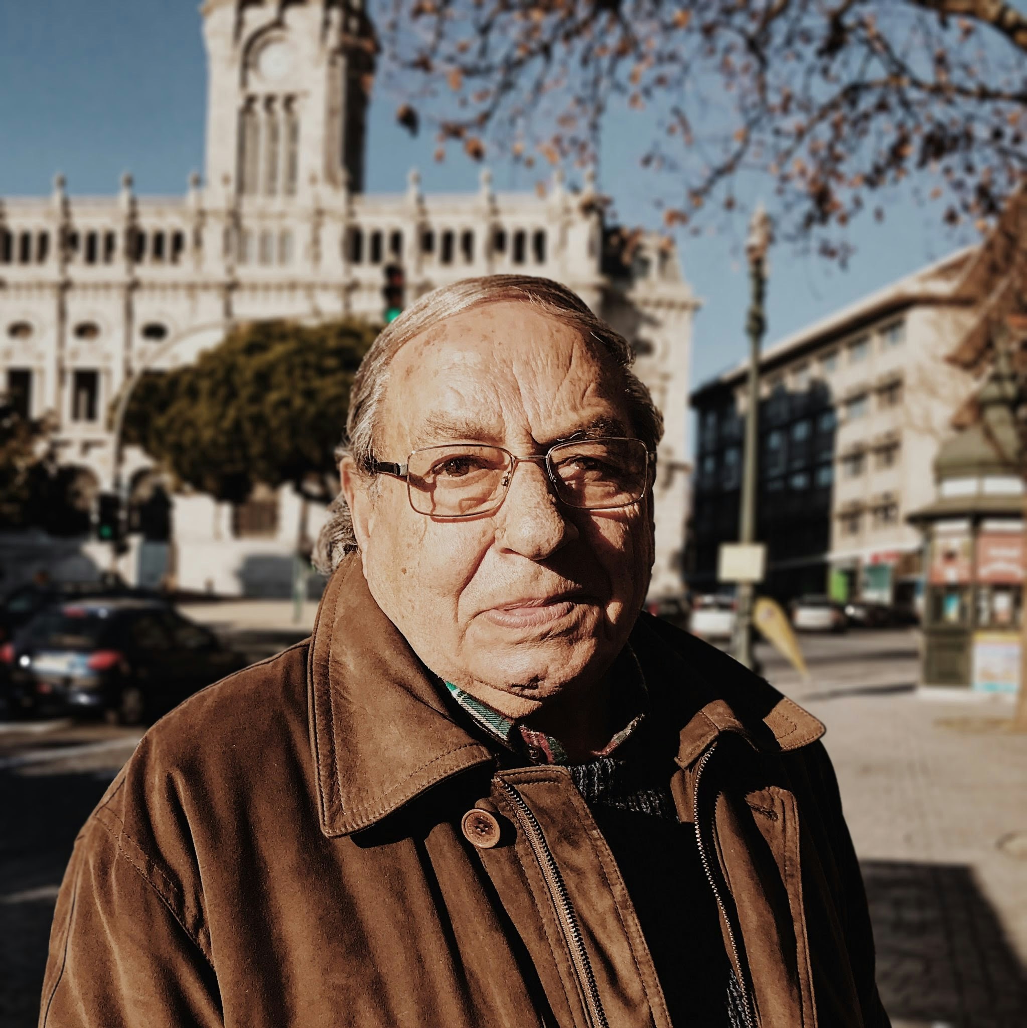 Headshot of man wearing glasses and a brown jacket