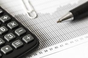 A close up black and white photograph of a calculator and a pen resting on a piece of paper.