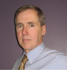 Headshot of Dan Manning. Dan is wearing a light blue shirt and a light colored tie while standing in front of a purple wall.