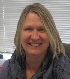 Joanne Sanders, Director of Finance, is wearing a purple shirt and scarf and seated in front of a window.