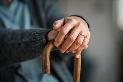 Elderly hands resting on wooden walking cane