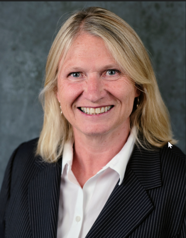 Joanne Sanders, Chief Financial Officer, smiling, with straight, shoulder-length blonde hair, wearing a dark pinstriped blazer over a white collared shirt, set against a plain gray background