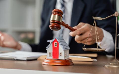 A judge strikes a gavel beside a small house model, symbolizing property law, housing disputes, or real estate judgment.