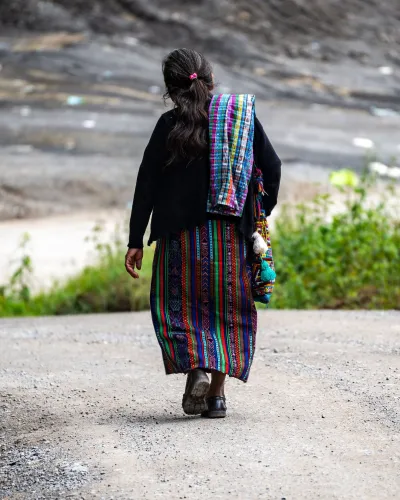 Guatemalan woman walking along a rural road in traditional clothing.