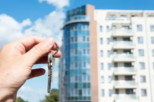 Hand holding a key in front of an apartment building