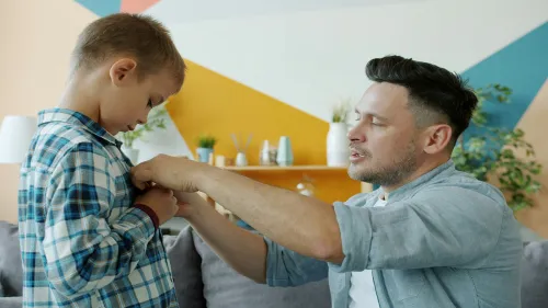 Father helping his young son button his shirt at home